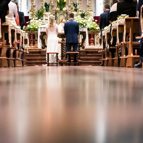Coppia di sposi durante la cerimonia in chiesa, vista dall'altare con decorazioni floreali, foto matrimoniali, reportage di matrimonio.