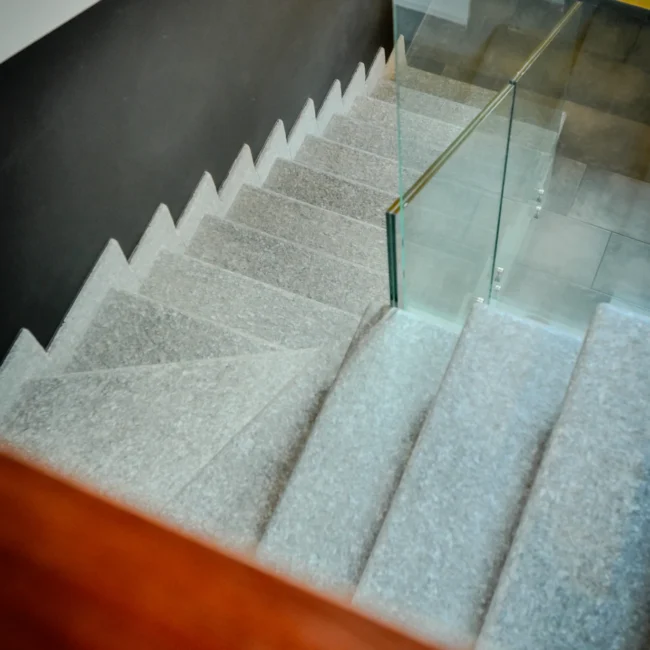 Foto immobili di una scala interna moderna con gradini in pietra e parapetto in vetro, illuminata da luce naturale, scattata da un fotografo per agenzia immobiliare.