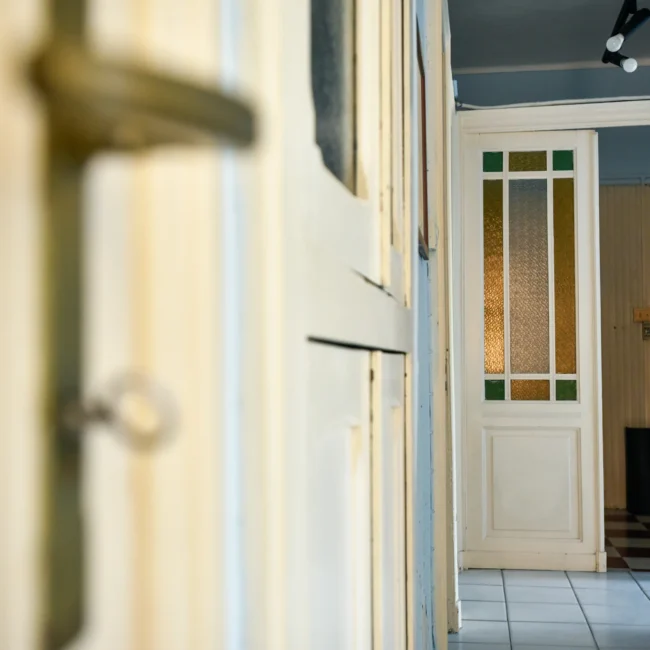Foto immobili di un corridoio interno con porte in legno e vetro colorato, pavimento a piastrelle bianche e nere, illuminazione moderna, scattata da un fotografo per agenzia immobiliare.