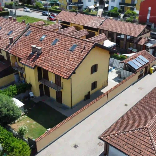 Riprese aeree con drone di una casa gialla con tetto rosso e cortile interno, ideale per un fotografo per agenzia immobiliare che promuove case moderne.
