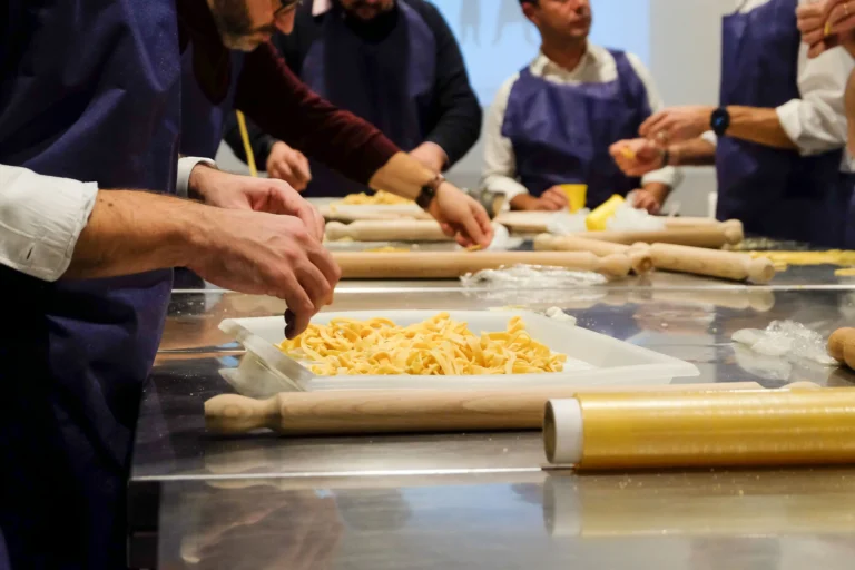 fotografo eventi Torino: Un gruppo di persone in un laboratorio di pasta fresca, che lavorano l'impasto con matterelli su un tavolo da cucina.