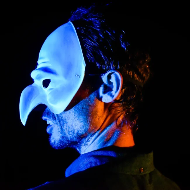 Uomo con maschera illuminata da luci blu e arancioni in un contesto teatrale, catturato dal fotografo eventi Torino.