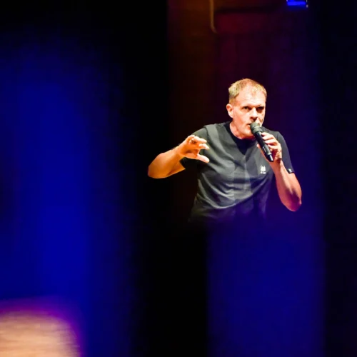 Fotografo eventi Torino fotografa stefano massini che parla con un microfono sotto luci blu su un palco minimalista.