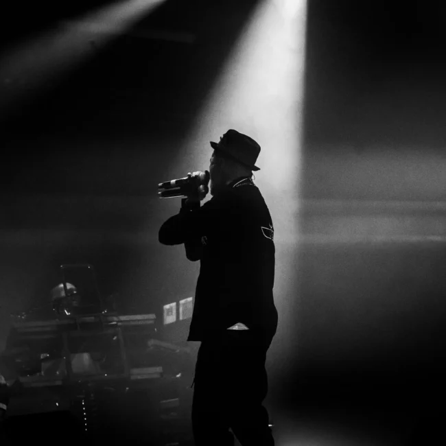 Fotografo eventi Torino cattura Samuel subsonica sul palco con un microfono, illuminato da un riflettore in un ambiente scuro.