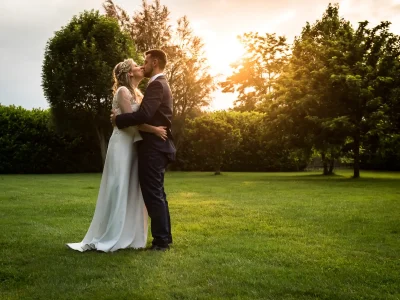 Reportage di matrimonio con una coppia di sposi che si abbraccia su un prato al tramonto, circondata da alberi e luce naturale.